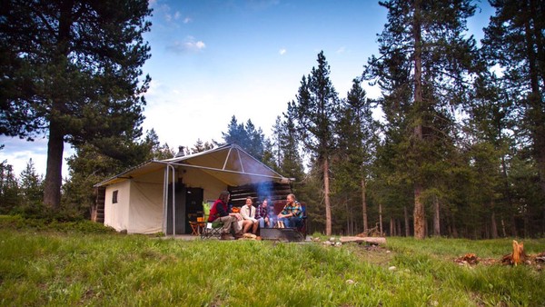 Campers enjoying a campfire in front of a canvas and log cabin